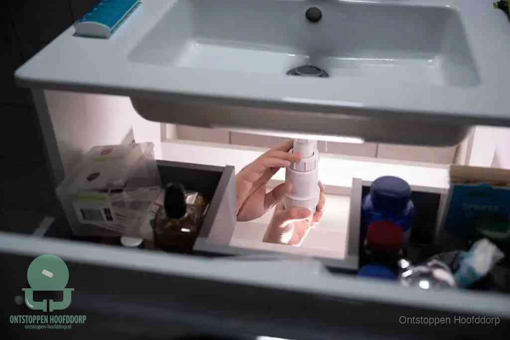 Een pompfles met zeep boven een wastafel, de heet water en afwasmiddel-methode om een vetprop in de afvoer los te maken in Hoofddorp