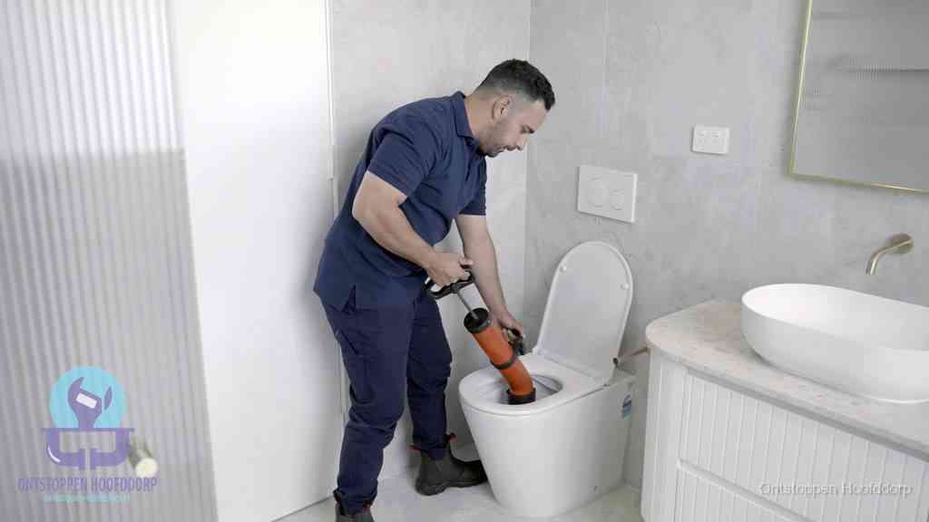Een monteur buigt over een wandcloset en duwt met de hand een persluchtontstopper in de toiletpot om de verstopping handmatig los te maken in Hoofddorp