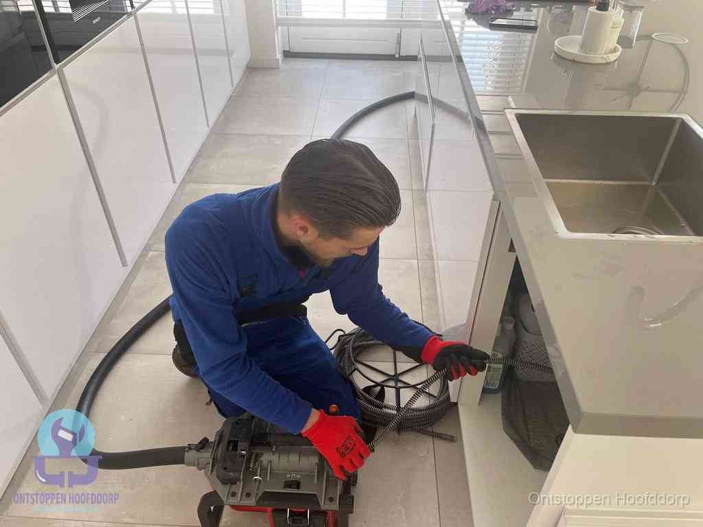 Een monteur ontstopt de keukenafvoer onder de spoelbak met een elektrische veermachine in Hoofddorp