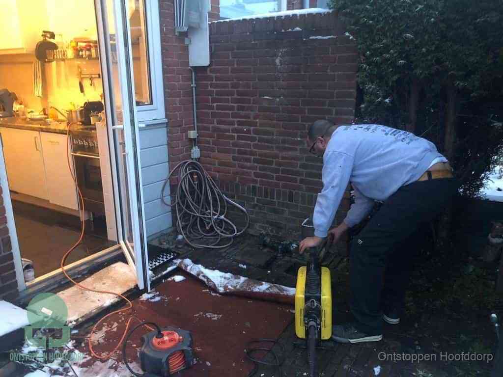 Een monteur werkt buiten bij een open riool-/grondput met een elektrische ontstoppingsmachine om een verborgen afvoerprobleem op te sporen in Hoofddorp