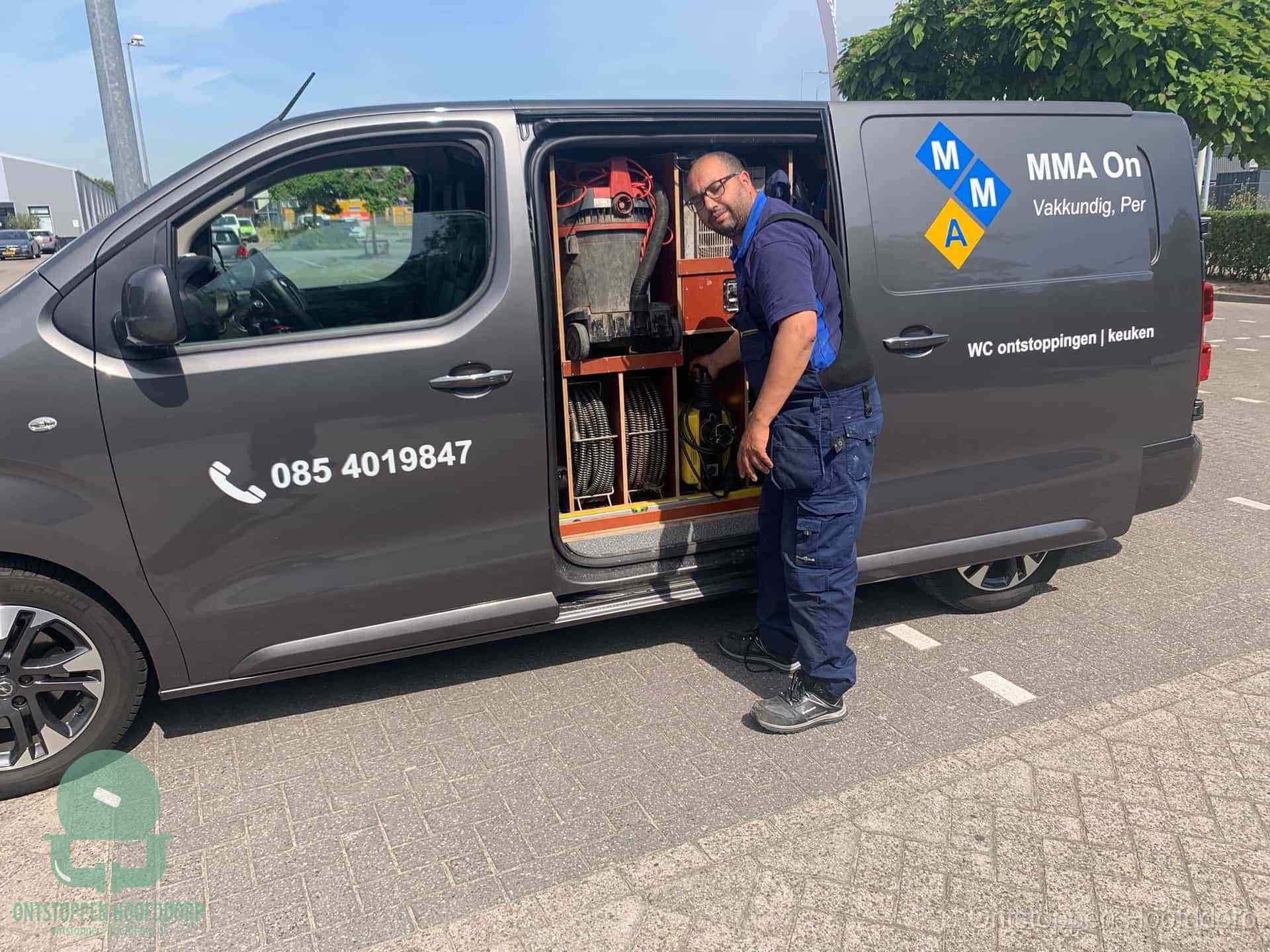 Een monteur bij de open schuifdeur van zijn bedrijfsbus op een parkeerplaats, klaar om de oorzaak van terugkerende afvoerverstoppingen aan te pakken in Hoofddorp