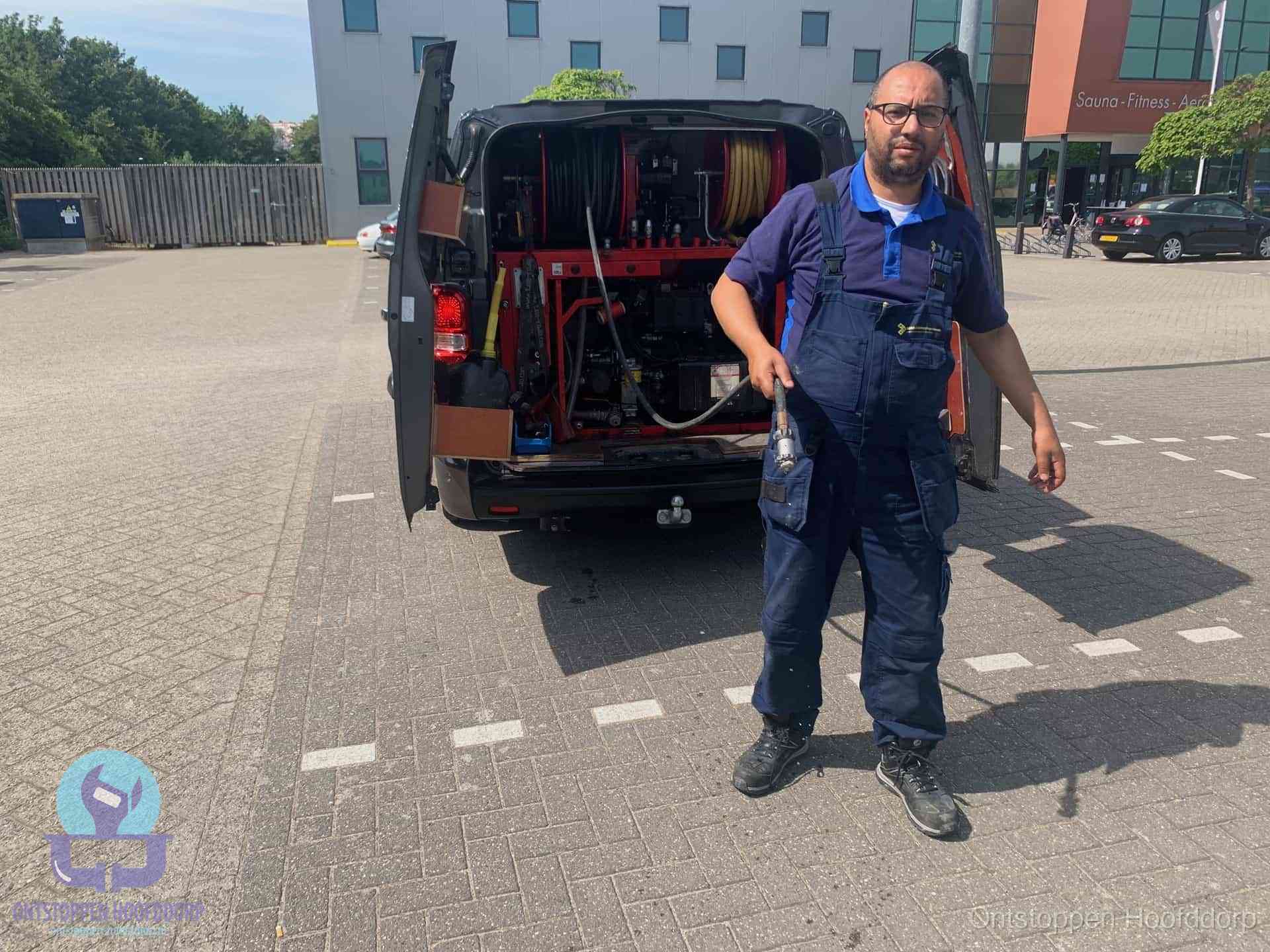 Een monteur bij zijn bestelbus met een hogedruk- en rioolreinigingsunit, klaar om de oorzaak van terugkerende wc-verstoppingen aan te pakken in Hoofddorp