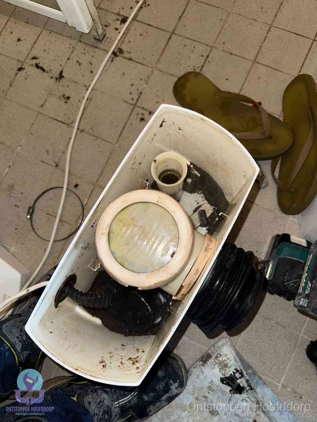 Een gedemonteerde toiletpot op de vloer met ontstoppingsveer en gereedschap ernaast, het verwijderen van een vastzittend voorwerp uit de wc in Hoofddorp