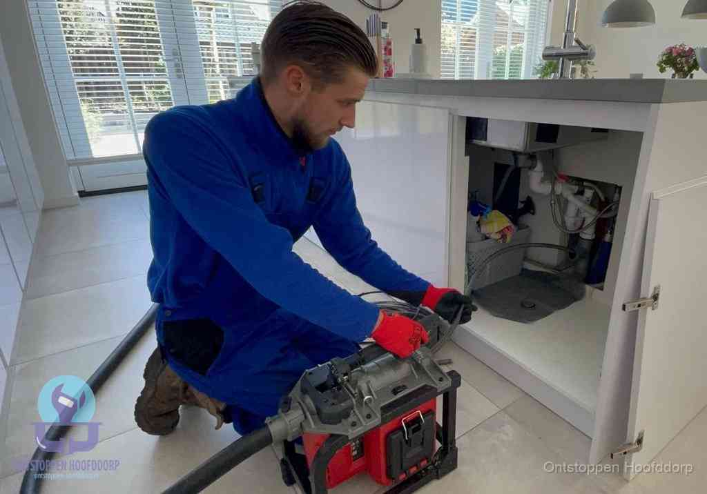 Een monteur voert een professionele elektrische ontstoppingsmachine in de afvoer onder de spoelbak tijdens het gootsteen ontstoppen in Hoofddorp