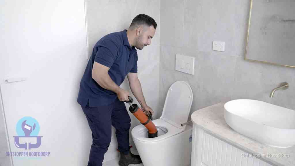 Een monteur gebruikt een handmatige perspomp (toiletontstopper) op een wandcloset tijdens het professioneel wc ontstoppen in Hoofddorp
