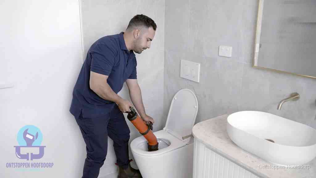 Een man gebruikt een handmatige luchtdruk-ontstopper in een modern betegeld toilet om zelf de wc te ontstoppen in Hoofddorp